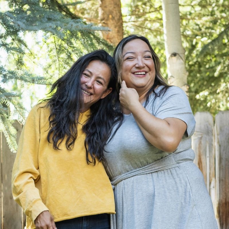 Two women smiling brightly while posing together for the camera, showcasing a moment of joy and friendship.